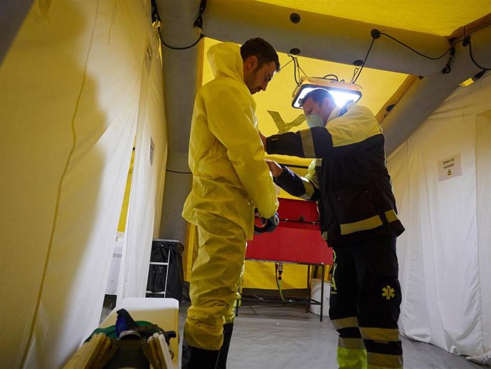 Un voluntario de la asociación sin ánimo de lucro DYA ayuda a otro para colocarse el traje protector antes de desinfectar las camillas colocadas en las inmediaciones del Complejo Hospitalario de Navarra prevenir la expansión del coronavirus. En Pamplona