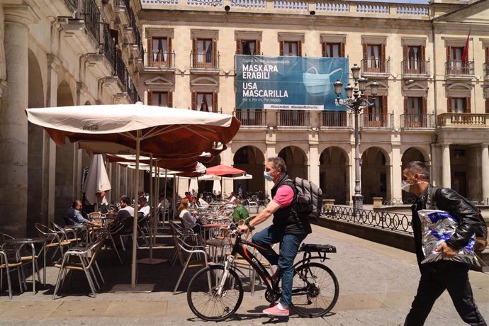 Un hombre con mascarilla pasea en bicicleta al lado de una terraza de una céntrica calle de Vitoria-Gasteiz, Álava
