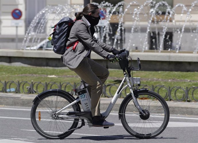 Un hombre protegido con mascarilla monta en una bicicleta de BiciMAD el primer día del uso obligatorio de mascarilla.