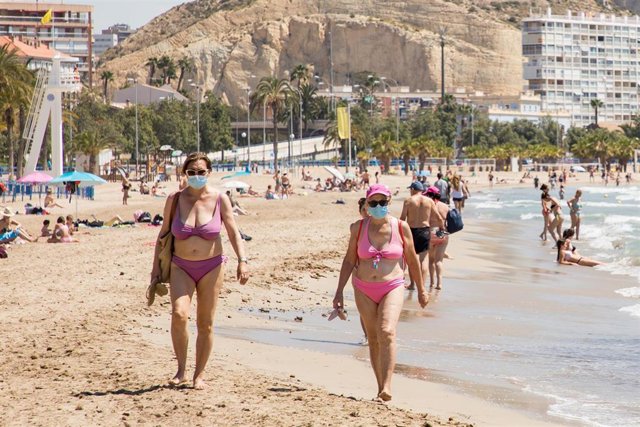 Dos mujeres protegidas con mascarilla pasean por la Playa del Postiguet 