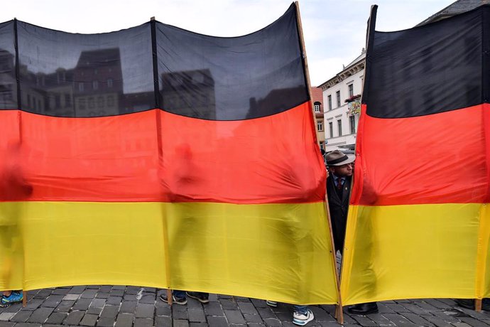Un hombre atisba entre la tela de una valla con los colores de la bandera de Alemania