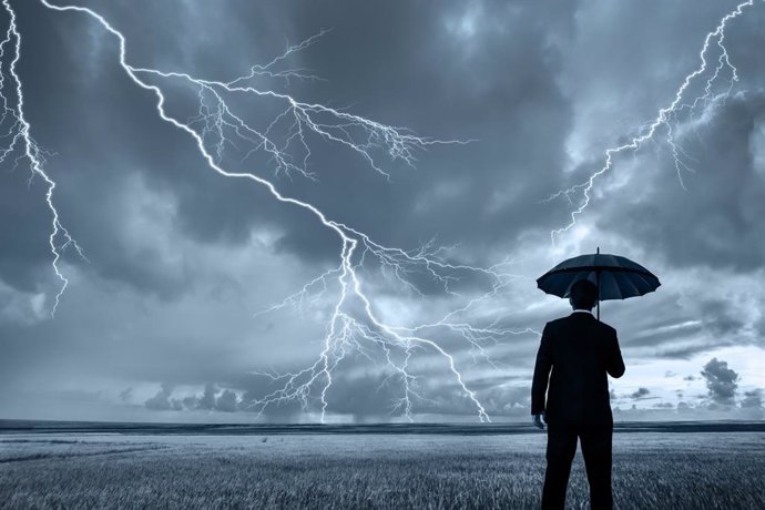 Un hombre con paraguas bajo la tormenta mientras caen los rayos.