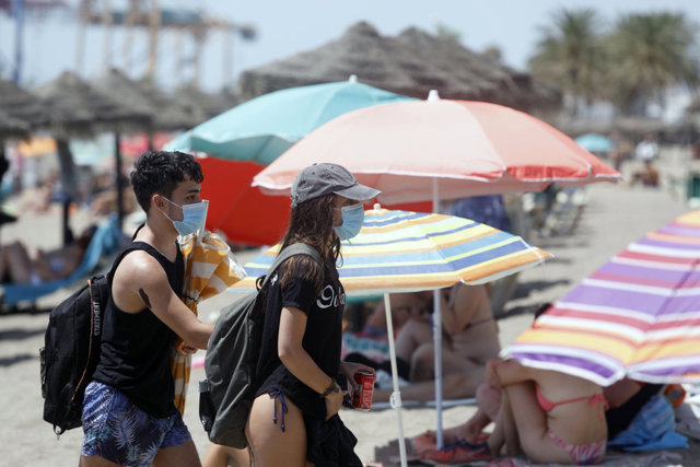 Dos personas con mascarillas mientras pasan entre sombrillas en la playa de La Malagueta. En Málaga