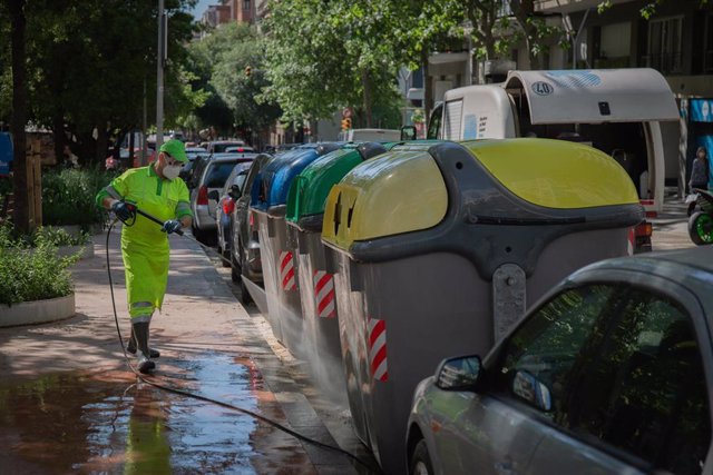 Un operario de limpieza del servicio municipal desinfectando un contenedor amarillo de basura