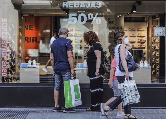 Varias personas observan objetivos del escaparate de una tienda con carteles indicativos de rebajas en Valencia