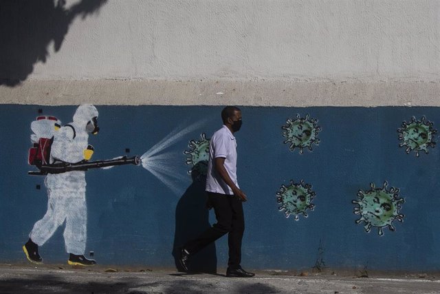 Un hombre con mascarilla camina delante de un mural sobre el coronavirus en Río de Janeiro