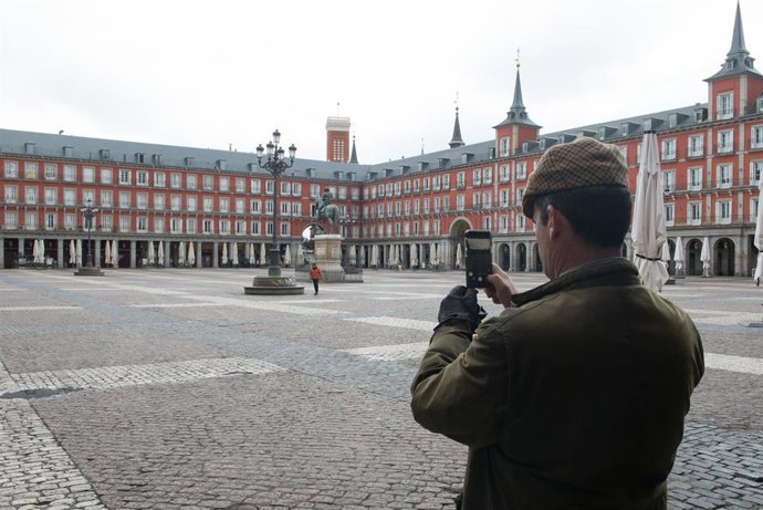 Un hombre hace una foto con su móvil a la céntrica Plaza Mayor de Madrid, vacía durante el estado de alarma decretado por el coronavirus, en Madrid (España)