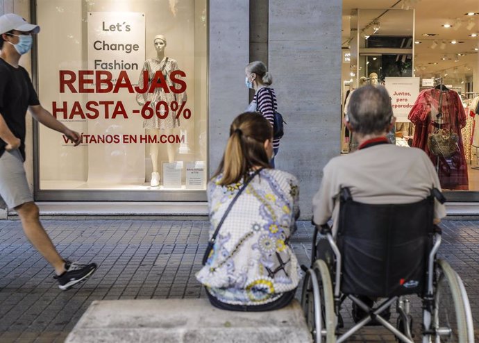 Varias personas pasan al lado del escaparate de una tienda donde se observan carteles indicativos de rebajas en Valencia, Comunidad Valenciana (España) a 3 de julio de 2020.