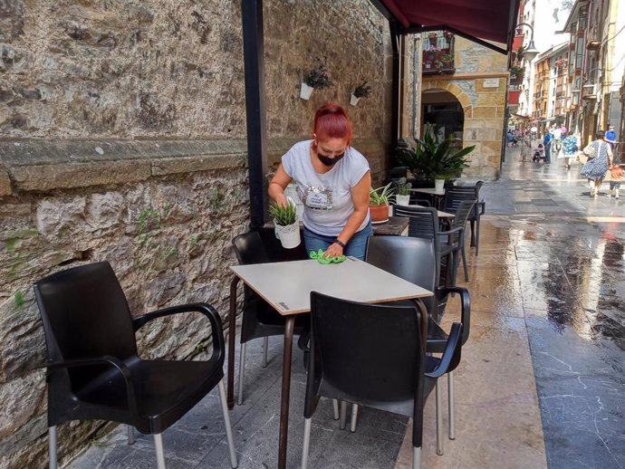 Una trabajadora desinfecta la mesa de la terraza de uno de los locales hosteleros que han vuelto a la fase 2 tras las limitaciones impuestas por el Gobierno Vasco. En Ermua, Vizcaya, País Vasco, (España), a 21 de julio de 2020.