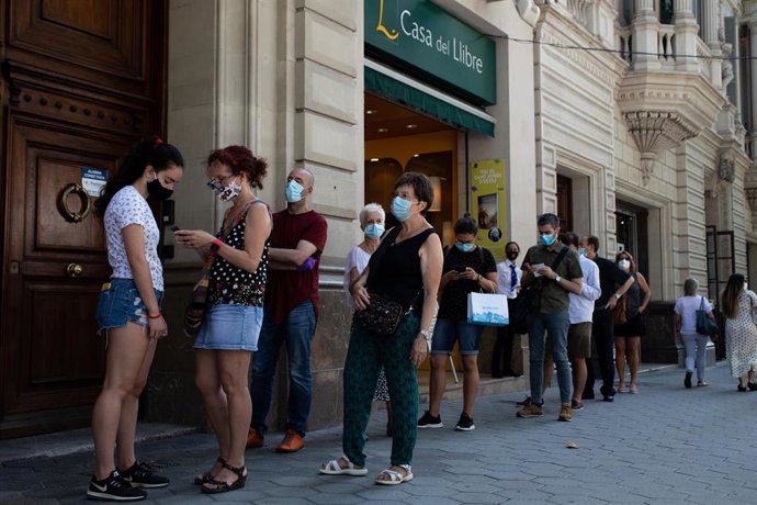 Decenas de personas protegidas con mascarilla hacen cola para entrar en una biblioteca, en Barcelona, Catalunya (España), a 23 de julio de 2020. Cataluña celebra este jueves un Día del Libro y de la Rosa aplazado tras no poder celebrarlo el pasado 23 de
