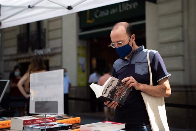Un hombre hojea un libro en un puesto de libros colocado en la calle, en Barcelona, Catalunya (España), a 23 de julio de 2020. (archivo)