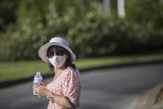 Una mujer, cubierta con sombrero, se refresca con agua.
