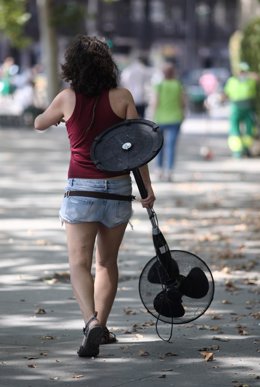 Una mujer pasea por una calle con un ventilador en la mano