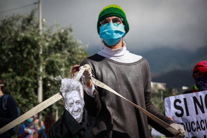 A man wearing a face mask and latex gloves holds a caricature image of Ecuadorian President Lenin Moreno during a protest against government-proposed cuts in the budget of the education sector amid the coronavirus pandemic