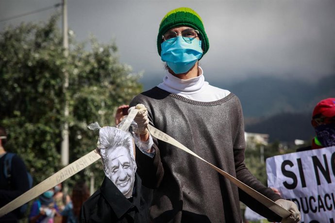 A man wearing a face mask and latex gloves holds a caricature image of Ecuadorian President Lenin Moreno during a protest against government-proposed cuts in the budget of the education sector amid the coronavirus pandemic