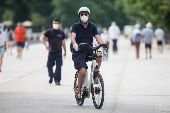 Un hombre protegido con mascarilla y guantes monta en una bicicleta BiciMAD en el parque de El Retiro.