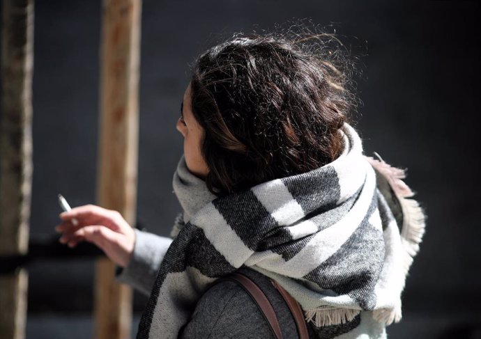 Una mujer abrigada con bufanda y abrigo, fumando durnate un día de viento por Madrid (España), a 8 de noviembre de 2019.