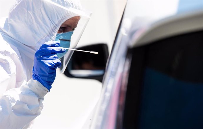 30 July 2020, Bavaria, Bergen: A health worker dressed in Personal Protective Equipment (PPE) takes a smear test from a car driver at a coronavirus (COVID-19) test centre on the motorway 8 (A8) at the Hochfelln-Nord rest area. Photo: Sven Hoppe/dpa