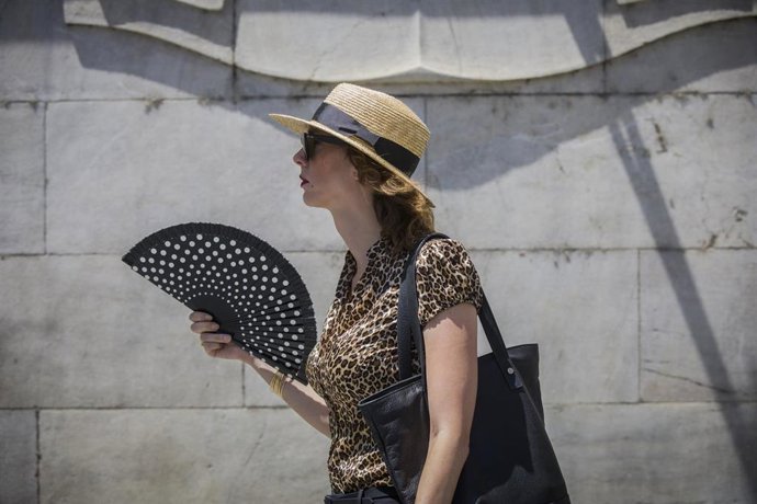 Una mujer se abanica mientras camina por la avd. de la Constitución durante la ola de calor africano que ha llegado este jueves a España. En Sevilla (Andalucía, España), a 30 de julio de 2020.