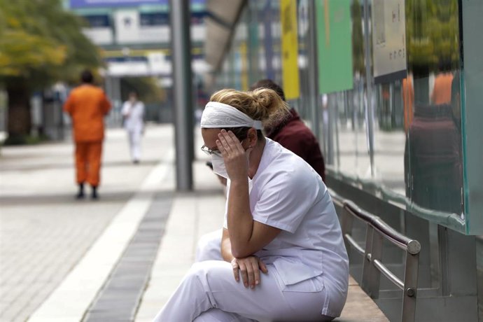 Una trabajadora sanitaria con mascarilla se sienta en un banco.