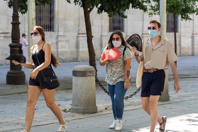 Tres jóvenes pasean con mascarillas y abanico en el primer día  de uso obligatorio de mascarillas en Sevilla. Foto de archivo