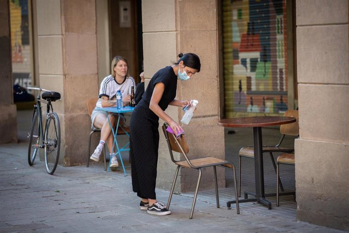 Una camarera limpia varias sillas y una mesa de la terraza de un bar, en Barcelona, Catalunya (España) a 26 de mayo de 2020.
