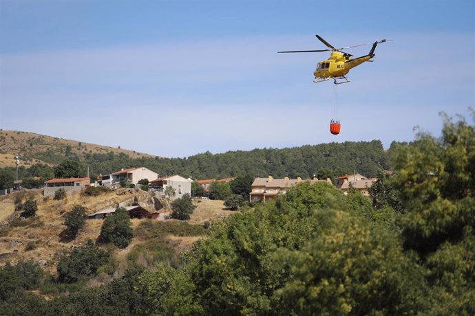 Un helicóptero transporta agua para vertirla sobre el incendio forestal originado en el término municipal de Robledo de Chavela (Madrid).
