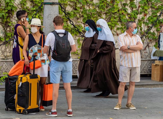 Unos turistas esperan el autobús mientras una pareja de monjas de la Orden de Santa Ángela de la Cruz  pasan por detrás con mascarillas el día que se ha anunciado la caída de un 98,9% de turistas extranjeros en Andalucía. Sevilla a 3 de agosto del 2020