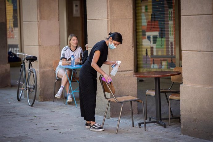 Una camarera limpia varias sillas y una mesa de la terraza de un bar en Barcelona