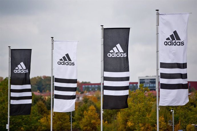 FILED - 15 October 2013, Bavaria, Herzogenaurach: Flags with the logos of the sporting goods manufacturer Adidas wave. Adidas' executive board member for global human resources, Karen Parkin, has stepped down after being accused of racism. Photo: Daniel