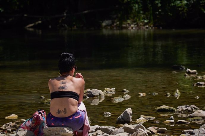 Una mujer disfruta sentada en la orilla del río Arga, en Pamplona