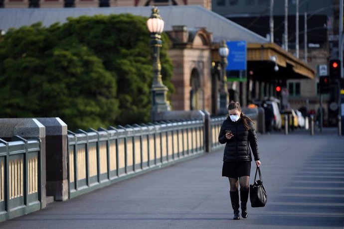 Una mujer transita una calle de Melbourne con una mascarilla puesta por el coronavirus. 
