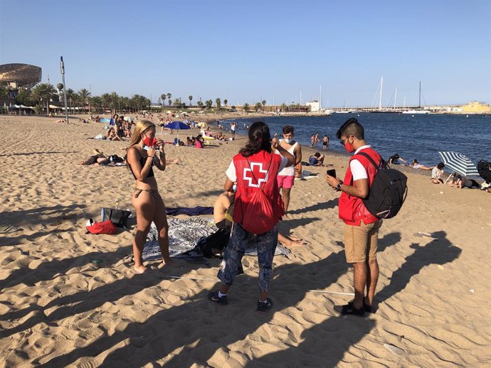 Dos joves voluntaris de Creu Vermella informen als seus parells de les mesures de prevenció contra el coronavirus, aquest divendres 7 d'agost del 2020 a la platja del Somorrostro de Barcelona.
