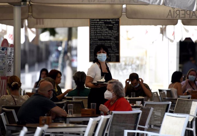 Una camarera con mascarilla atiende a los clientes en una terraza de un bar el día en el que entra en vigor en la Comunidad de Madrid la ampliación del uso obligatorio de la mascarilla, la limitación de las reuniones en terrazas a grupos de un máximo de