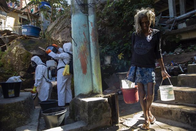 Una mujer transporta unos cubos con agua mientras unos voluntarios de los servicios de salud realizan labores de desinfección en una favela en el barrio de Botafogo, en Río de Janeiro.
