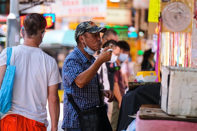 Un señor disfruta de un bocado en medio de la calle después de que las autoridades de Hong Kong hayan decretado el cierre de establecimientos donde se sirve comida debido a la tercera ola de contagios por la COVID-19 que sufre la región.