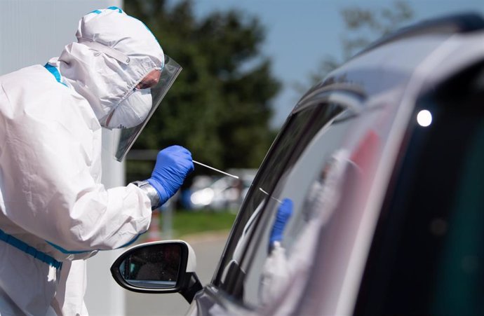 09 August 2020, Bavaria, Bergen: A health care worker of the Bavarian Red Cross in a protective takes a smear test from a car driver at a coronavirus  (COVID-19) test centre on the motorway 8 (A8) at the Hochfelln-Nord rest area. Photo: Sven Hoppe/dpa