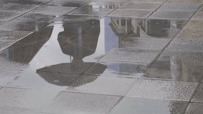 Una persona con paraguas se refleja en un charco provocado por la lluvia  en Bilbao.