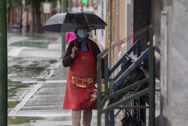 Una mujer se protege de la lluvia bajo su paraguas durante una tormenta en una imagen de archivo.