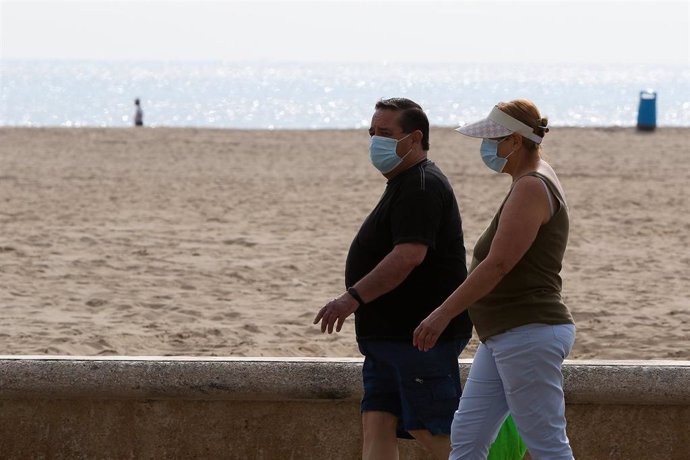 Dos personas protegidas con mascarilla pasean por la playa de la Malvarrosa