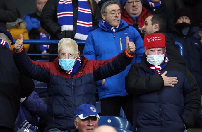 12 March 2020,Glasgow: Fan wearing the facemasks of UK Prime Minister Boris Johnson and US President Donald Trump in the stands during the UEFA Europa League round of 16 first leg soccer match between Rangers and Bayer Leverkusen at Ibrox Stadium.