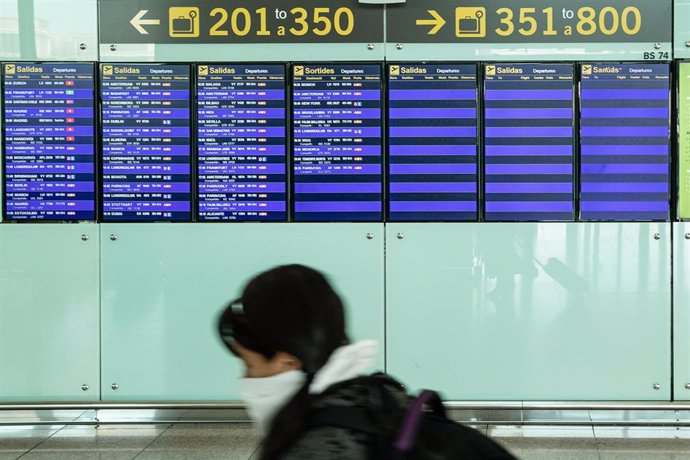 Una pasajera con mascarilla observa los paneles del aeropuerto El Prat de Barcelona durante el sexto día de confinamiento tras la declaración del estado de alarma por la pandemia de coronavirus, en Barcelona / Cataluña (España), a 20 de marzo de 2020.