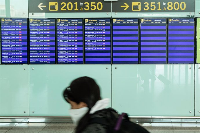 Una passatgera amb mascarilla observa els panells de l'aeroport El Prat de Barcelona durant el sis dia de confinament després de la declaració de l'estat d'alarma per la pandmia de coronavirus, a Barcelona / Catalunya (Espanya), a 20 de mar de 2020.