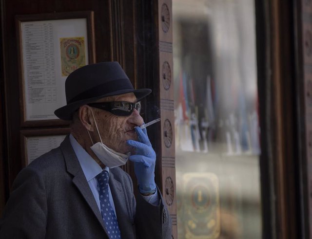 Un hombre con mascarilla y guantes fumando un cigarro durante el quinto día de la fase 2 en Sevilla (Andalucía, España), a 29 de mayo de 2020.