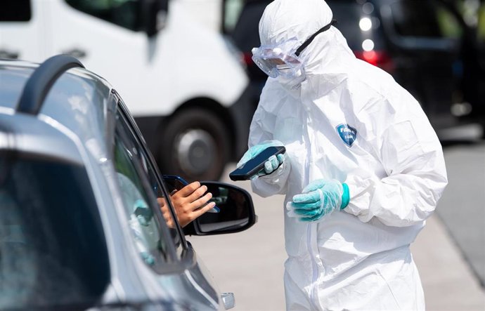 14 August 2020, Bavaria, Kiefersfelden: A health care worker of Eurofins Scientific in a protective suit holds a scanner in his hands at a coronavirus  (COVID-19) test centre on the motorway 93 (A93). Photo: Sven Hoppe/dpa