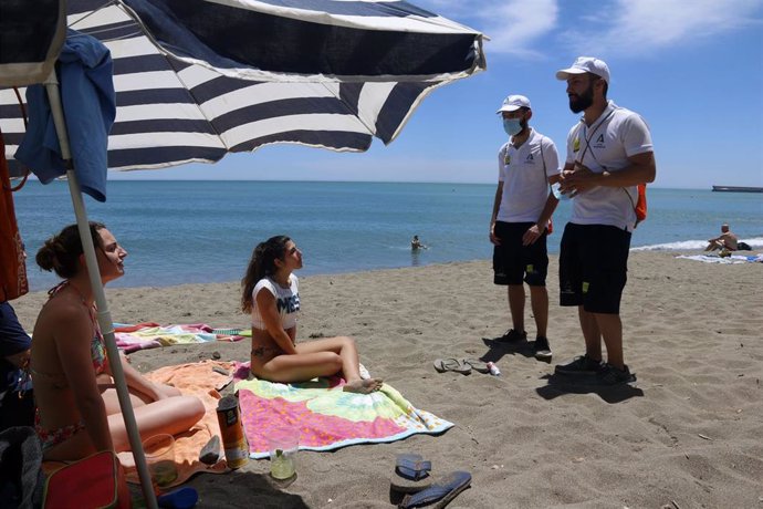 Una pareja de auxiliares de la playa de Andalucía asesoran a bañistas sobre las medidas preventivas sobre el COVID-19 en la playa de La Malagueta. Málaga a 16 de junio del 2020