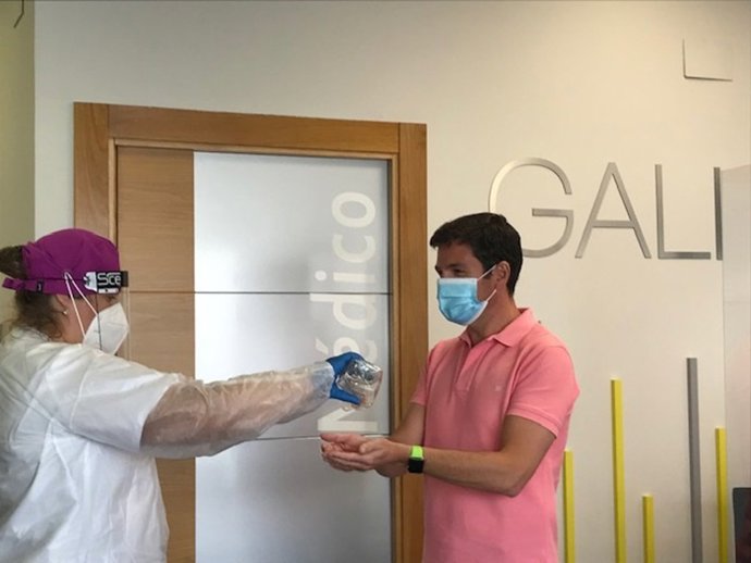 Una trabajadora ofrece gel hidroalcohólico a otro.