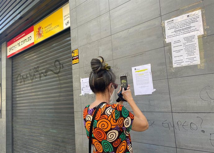 Una mujer fotografía uno de los carteles con instrucciones para hacer trámites por internet colocados en la fachada de una oficina del SEPE