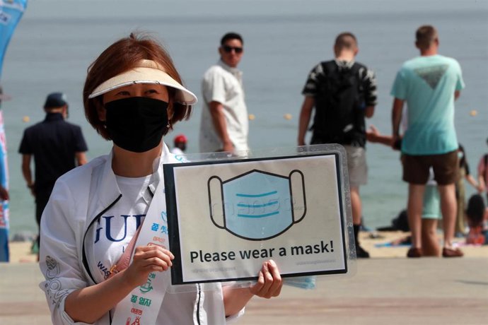 Una mujer sostiene un cartel en el que se pide utilizar la mascarilla para evitar más contagios durante la crisis sanitaria de la pandemia.