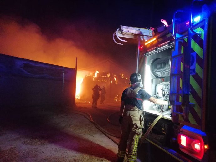 Bomberos trabajan en la extinción de un incendio declarado en un almacén de paja de Lorca
